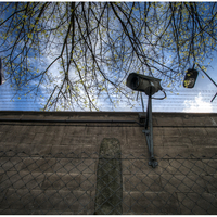 Outside the prison wall, a fence in front and surveillance camera.